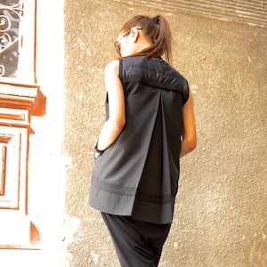 May include: A woman wearing a black sleeveless top with a pleated back and black pants. She is wearing black sandals with white soles.