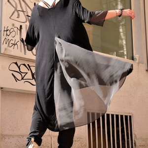 May include: A person wearing a black tunic with a sheer overlay and black pants. The tunic has a long, flowing design and the person is wearing a black headband.