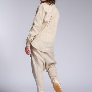 May include: A woman wearing a light beige linen shirt and pants. She is wearing white sneakers with a brown sole. The woman is standing on a white background.