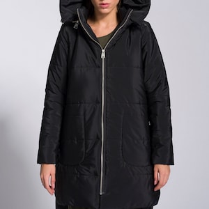 May include: A black hooded puffer jacket with a zipper closure. The jacket has a long, slightly asymmetrical hemline and a relaxed fit.