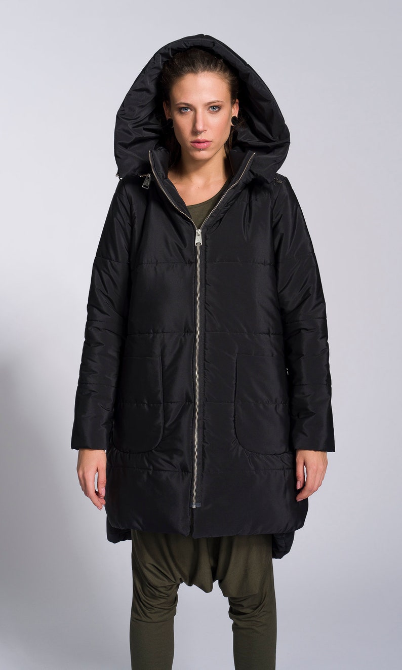 May include: A black hooded puffer jacket with a zipper closure. The jacket has a long, slightly asymmetrical hemline and a relaxed fit.