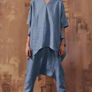 May include: A light blue linen top with a v-neck and short sleeves paired with matching light blue linen pants. The pants have a loose, baggy fit and are cropped at the ankles. The model is wearing white sneakers with green and blue accents.
