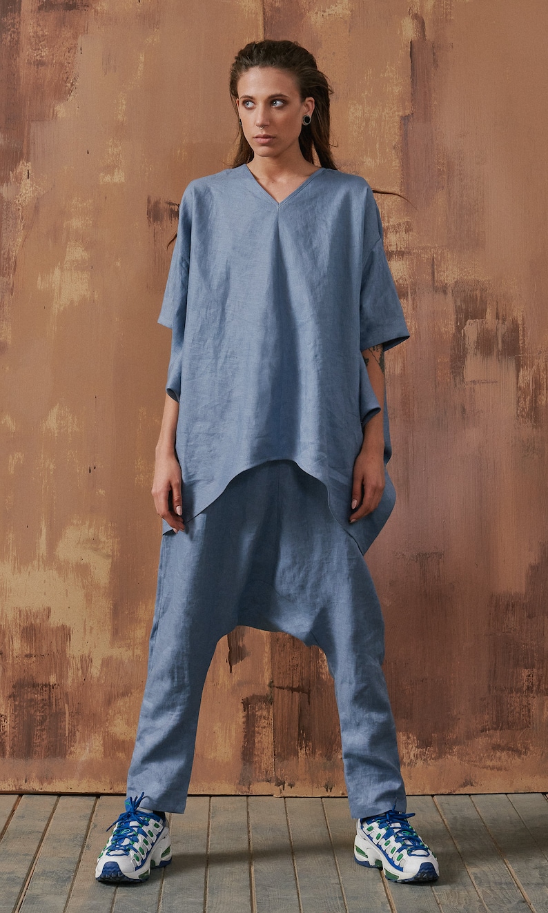 May include: A light blue linen top with a v-neck and short sleeves paired with matching light blue linen pants. The pants have a loose, baggy fit and are cropped at the ankles. The model is wearing white sneakers with green and blue accents.