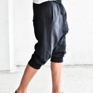 May include: Black cropped pants with a drawstring waist and a loose, baggy fit. The pants have a unique design with a curved seam on the front and a pocket on the side.