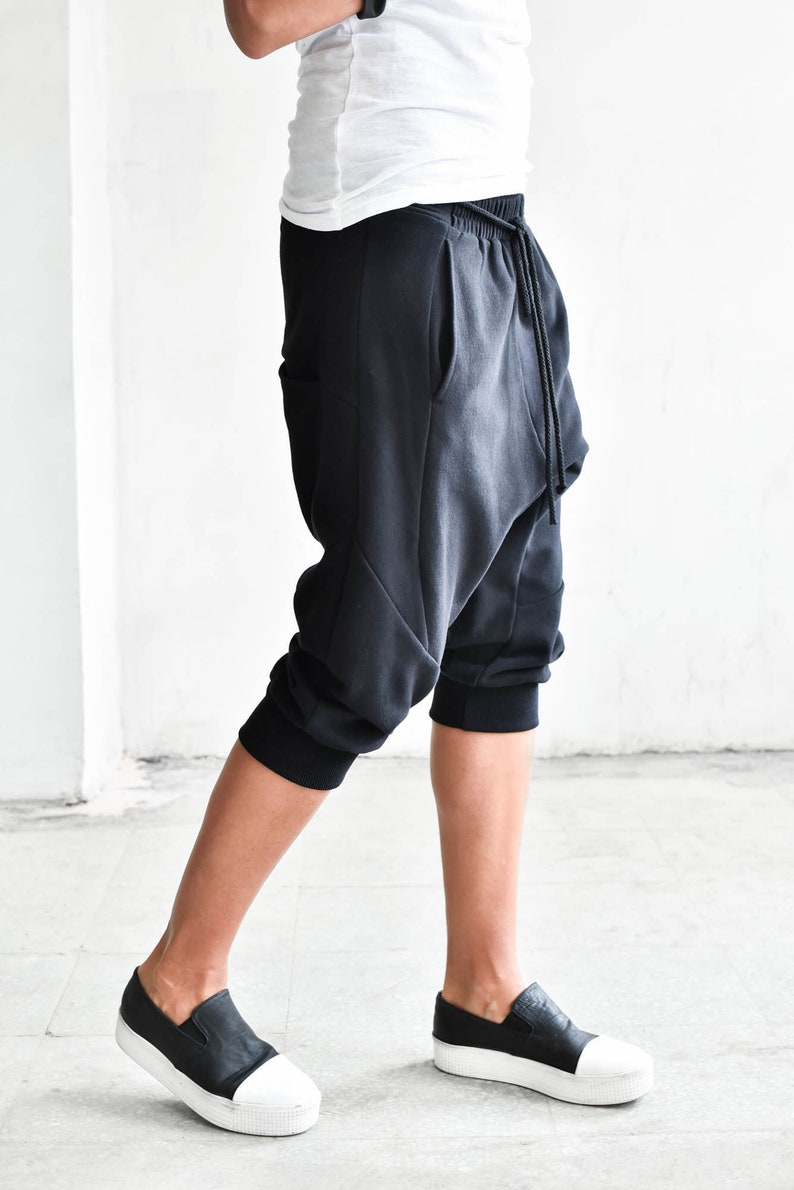 May include: Black cropped pants with a drawstring waist and a loose, baggy fit. The pants have a unique design with a curved seam on the front and a pocket on the side.