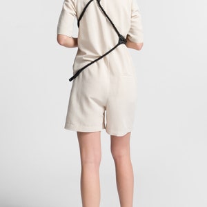 May include: A white jumpsuit with a black rope detail across the back. The model is wearing neon green and black trainers.