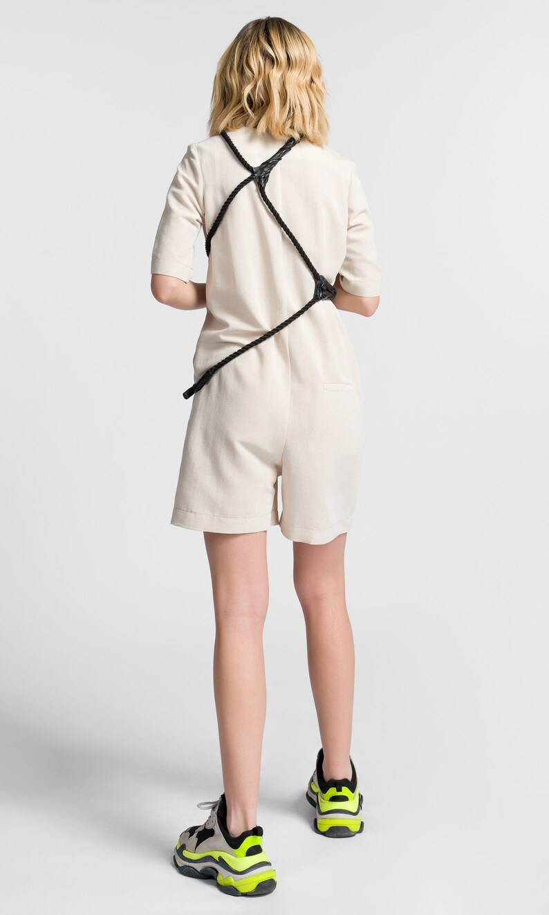 May include: A white jumpsuit with a black rope detail across the back. The model is wearing neon green and black trainers.