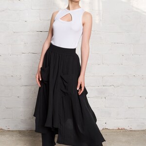 Pode incluir: Uma mulher vestindo um top branco sem mangas com um decote de fechadura e uma saia preta assim&eacute;trica com bolsos. Ela est&aacute; usando t&ecirc;nis preto e branco com detalhes vermelhos.