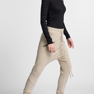 Puede incluir: Una mujer lleva una camisa negra de manga larga y pantalones beige con un dise&ntilde;o &uacute;nico. Lleva zapatillas negras de ca&ntilde;a alta con suela gruesa.