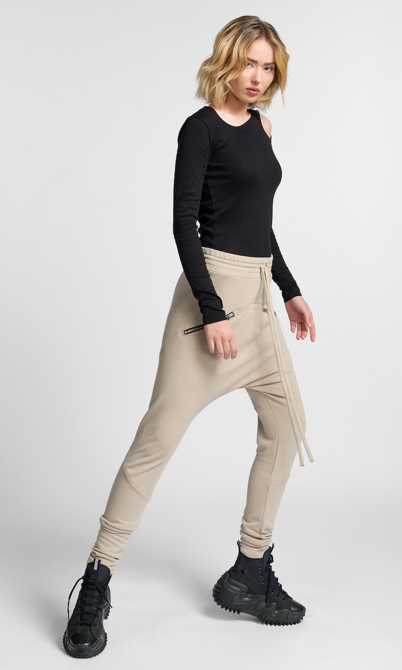 Puede incluir: Una mujer lleva una camisa negra de manga larga y pantalones beige con un dise&ntilde;o &uacute;nico. Lleva zapatillas negras de ca&ntilde;a alta con suela gruesa.