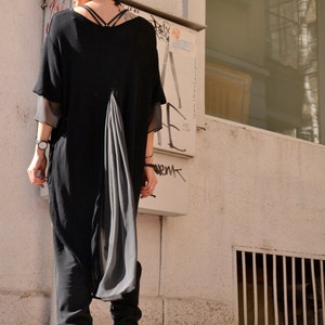 May include: A woman wearing a black long-sleeved tunic with a flowing grey panel in the back. She is wearing a black headband and white boots.