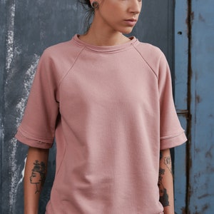 Op de afbeelding: Een roze, korte mouwen sweatshirt met een distressed zoom en raglan mouwen. Het sweatshirt is gemaakt van een zachte, comfortabele stof en heeft een ontspannen pasvorm.