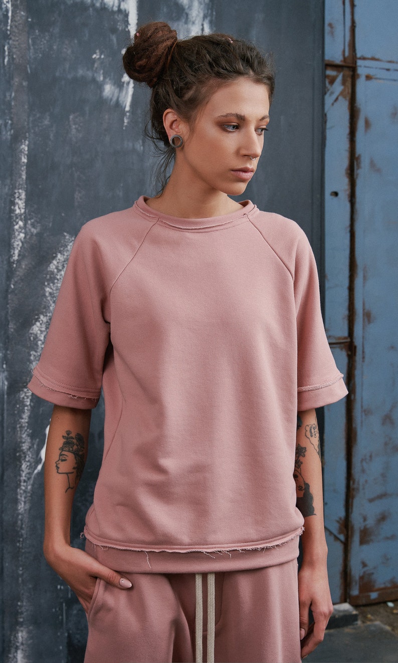 Op de afbeelding: Een roze, korte mouwen sweatshirt met een distressed zoom en raglan mouwen. Het sweatshirt is gemaakt van een zachte, comfortabele stof en heeft een ontspannen pasvorm.