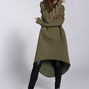 May include: A long, olive green hooded sweatshirt with a high-low hemline. The sweatshirt has a large kangaroo pocket and long sleeves. The model is wearing black leggings and black high-top sneakers.