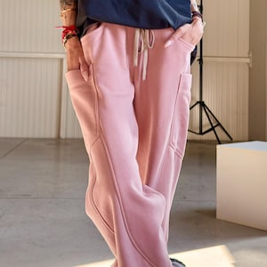 May include: A navy blue t-shirt with white text and pink sweatpants. The sweatpants have pockets and a drawstring. The text on the shirt reads "New Edition Tokyo 09 2 Sydney 10 13". The outfit is paired with gray sneakers.