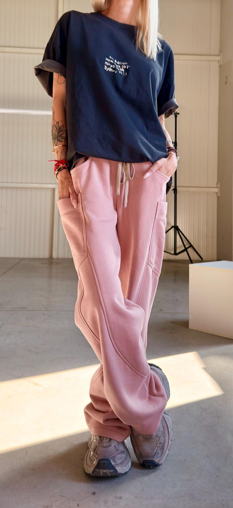May include: A navy blue t-shirt with white text and pink sweatpants. The sweatpants have pockets and a drawstring. The text on the shirt reads "New Edition Tokyo 09 2 Sydney 10 13". The outfit is paired with gray sneakers.