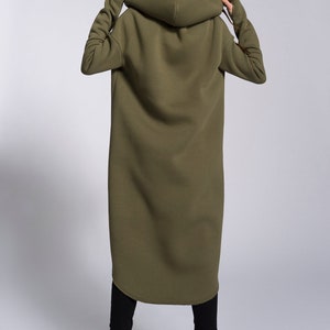 May include: A long, olive green hooded sweatshirt with a relaxed fit. The sweatshirt has large hood and long sleeves.