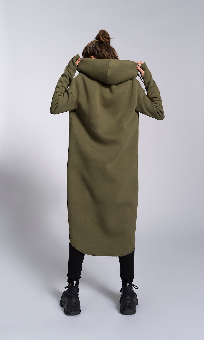 May include: A long, olive green hooded sweatshirt with a relaxed fit. The sweatshirt has large hood and long sleeves.