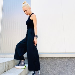 May include: A person wearing black wide-leg pants and a black tank top with a white belt. They are wearing black and grey high-top sneakers with a neon green accent.