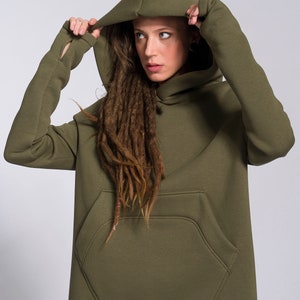 May include: A long, olive green hooded sweatshirt with a large front pocket. The hood is pulled up and the sweatshirt has big kangaroo pocket  in front