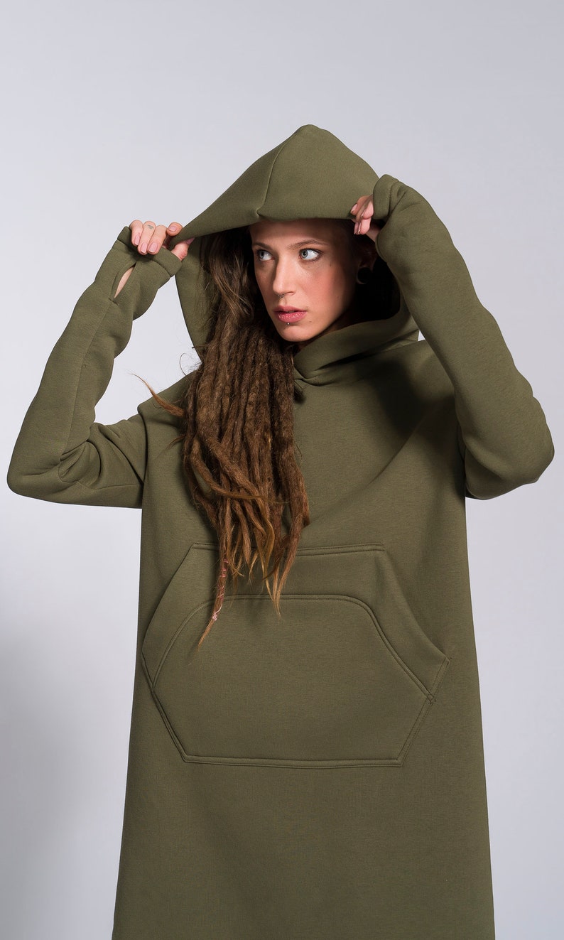 May include: A long, olive green hooded sweatshirt with a large front pocket. The hood is pulled up and the sweatshirt has big kangaroo pocket  in front