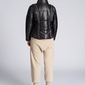 May include: A black puffer jacket with a high collar and zipper details, paired with beige sweatpants and high-top sneakers. The sneakers are black and white with a star design.