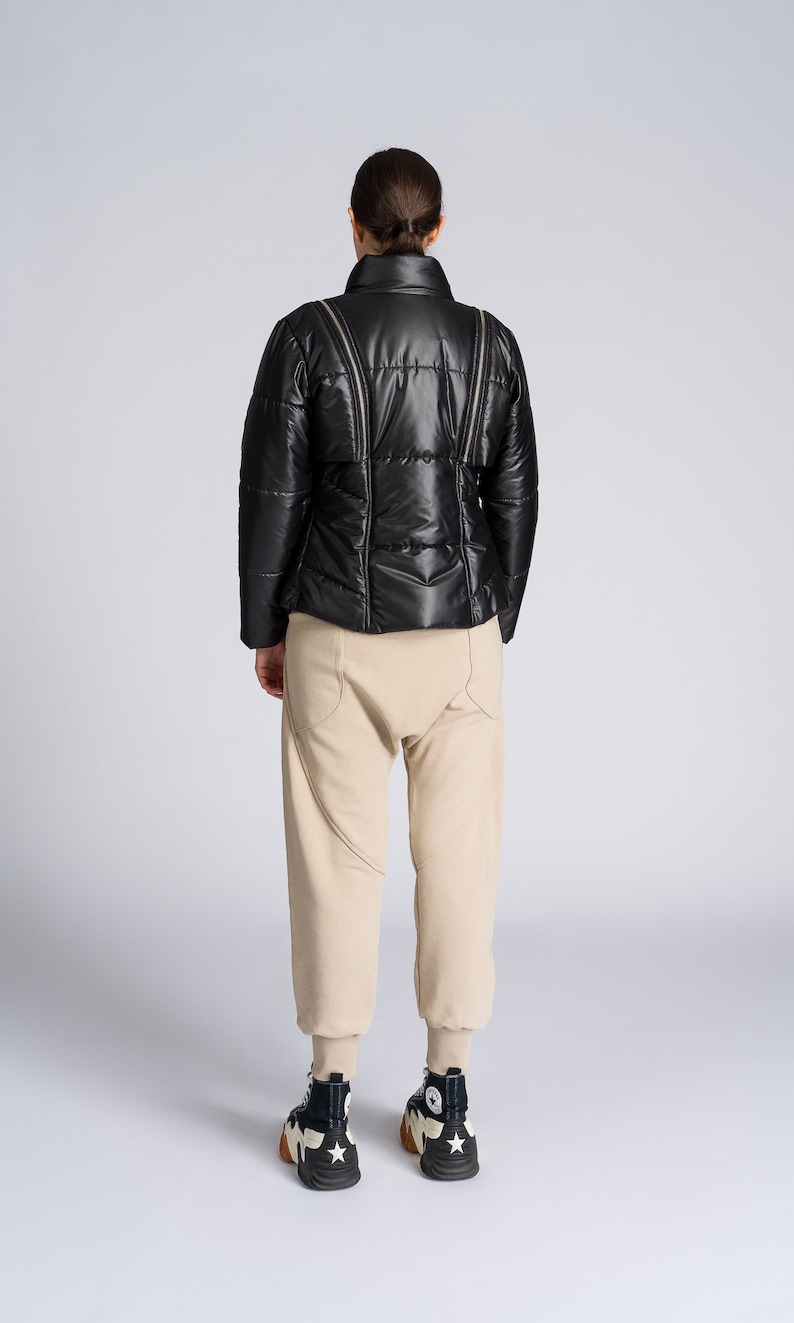 May include: A black puffer jacket with a high collar and zipper details, paired with beige sweatpants and high-top sneakers. The sneakers are black and white with a star design.