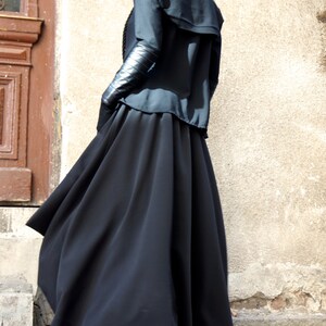 May include: A woman wearing a black long-sleeved top with a black skirt and black heeled sandals. The skirt is flowing and the top has a collar.