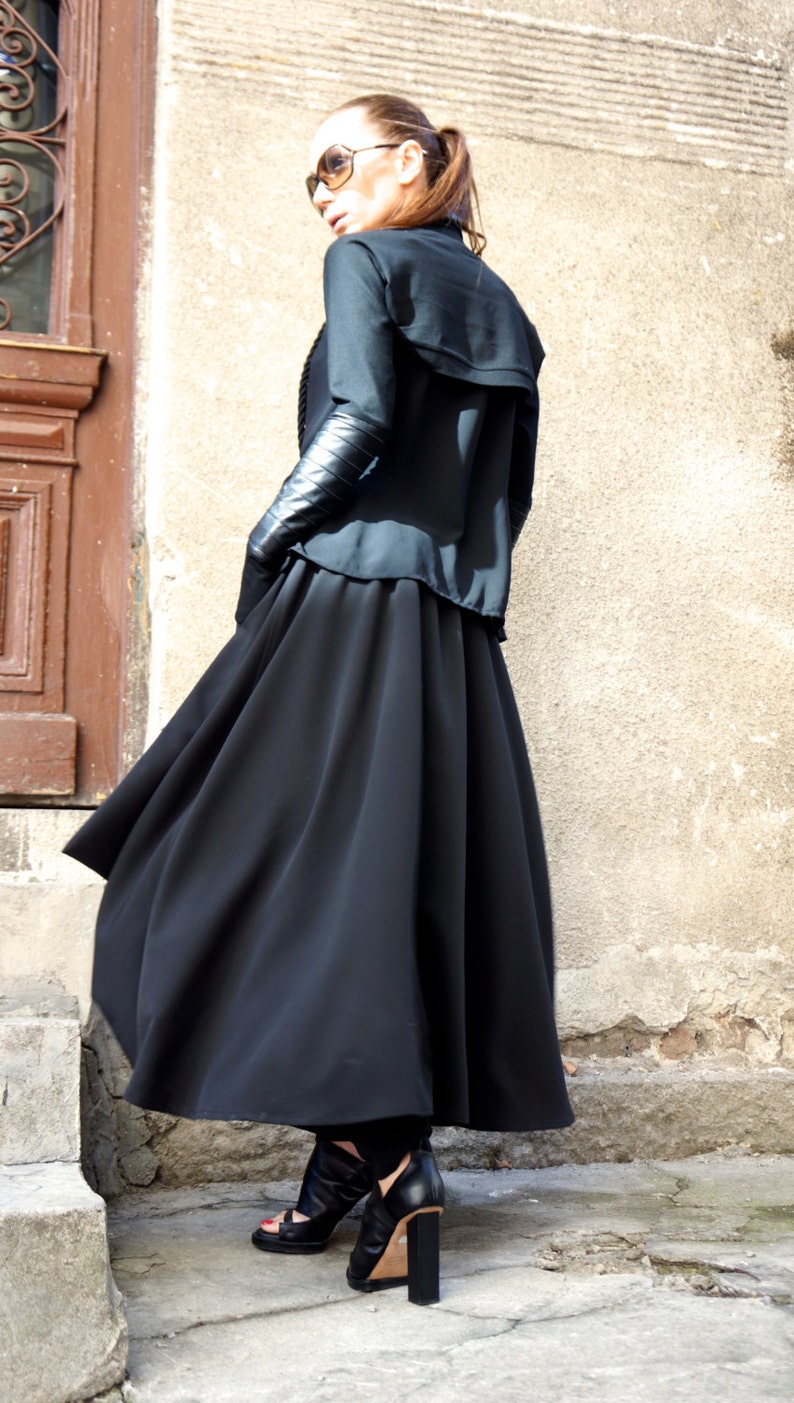 May include: A woman wearing a black long-sleeved top with a black skirt and black heeled sandals. The skirt is flowing and the top has a collar.