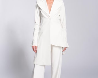 May include: A white blazer with a long, asymmetrical hemline and a single button closure. The blazer is worn with white trousers and white trainers.