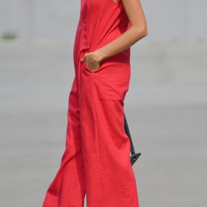 May include: A woman wearing a sleeveless red jumpsuit with a V-neckline. The jumpsuit has a button closure and pockets.