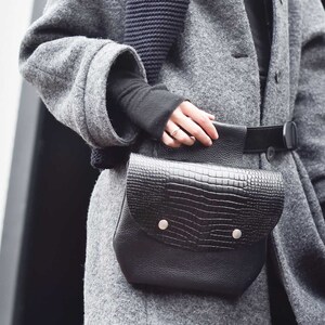 May include: A grey wool coat with a black knitted scarf and a black leather crossbody bag with a crocodile pattern.