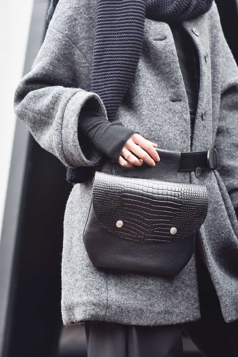 May include: A grey wool coat with a black knitted scarf and a black leather crossbody bag with a crocodile pattern.