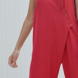 May include: A red sleeveless jumpsuit with a wrap-style neckline and a single button closure on the side.