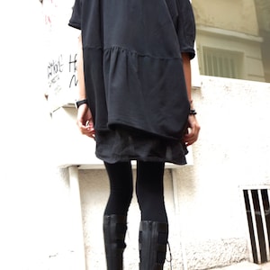 Puede incluir: Una mujer con una t&uacute;nica negra holgada con cintura fruncida, leggings negros y botas de plataforma negras.