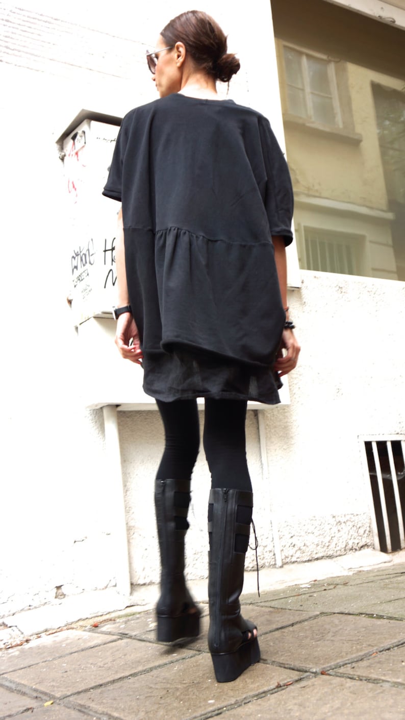 Puede incluir: Una mujer con una t&uacute;nica negra holgada con cintura fruncida, leggings negros y botas de plataforma negras.