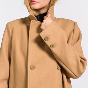 May include: A camel-colored double-breasted coat with a high collar. The coat has a smooth texture and is made of a soft material.