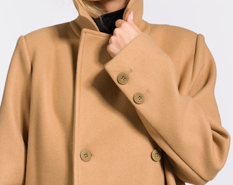 May include: A camel-colored double-breasted coat with a high collar. The coat has a smooth texture and is made of a soft material.