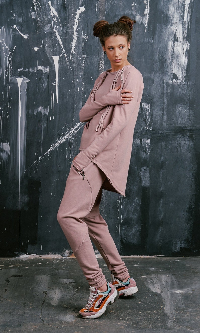 Peut inclure: Une femme portant un haut asym&eacute;trique rose &agrave; manches longues et un pantalon assorti. Elle porte des baskets avec des accents orange, blanc et bleu.