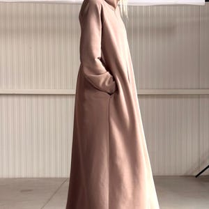 May include: A long, hooded, taupe-colored coat with pockets. The coat is floor-length and made of a soft material. The hood is large and drapes over the shoulders. A stylish and comfortable outerwear garment.