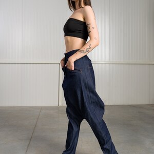 K&ouml;nnte beinhalten: Eine Frau tr&auml;gt ein schwarzes Crop-Top und eine dunkelblaue Jeanshose mit einem einzigartigen, weiten Design. Sie tr&auml;gt schwarze Sneaker mit einer dicken Sohle.