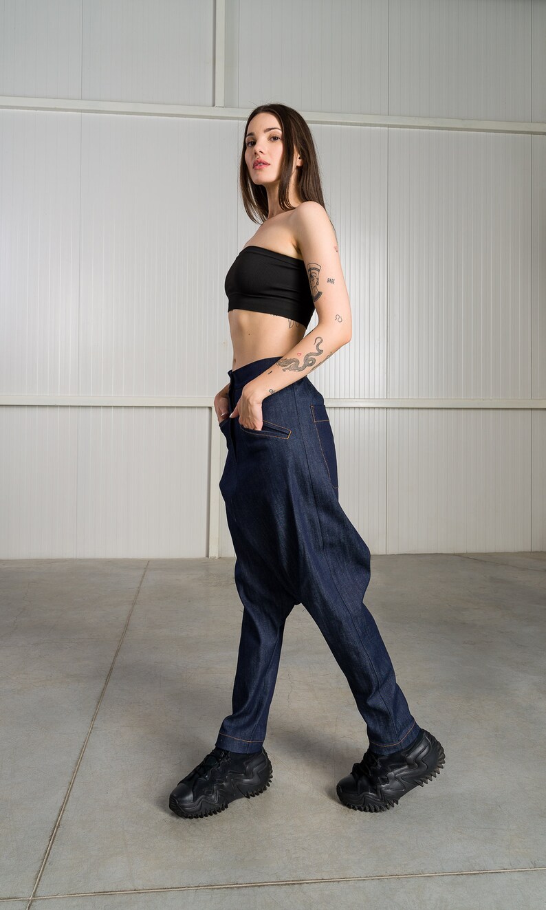 K&ouml;nnte beinhalten: Eine Frau tr&auml;gt ein schwarzes Crop-Top und eine dunkelblaue Jeanshose mit einem einzigartigen, weiten Design. Sie tr&auml;gt schwarze Sneaker mit einer dicken Sohle.