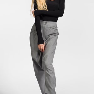 May include: A woman wearing a black long-sleeved shirt with a cut-out detail at the neckline and gray pants. She is wearing black boots with white laces that say "love" on them.