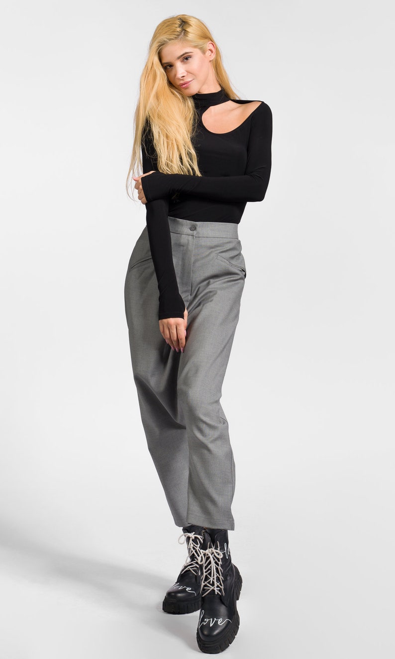 May include: A woman wearing a black long-sleeved shirt with a cut-out detail at the neckline and gray pants. She is wearing black boots with white laces that say "love" on them.
