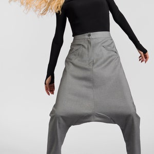 May include: A woman wearing a black long-sleeved shirt with a cut-out neckline and gray, loose-fitting pants. She is wearing black shoes with the word "love" written on them.