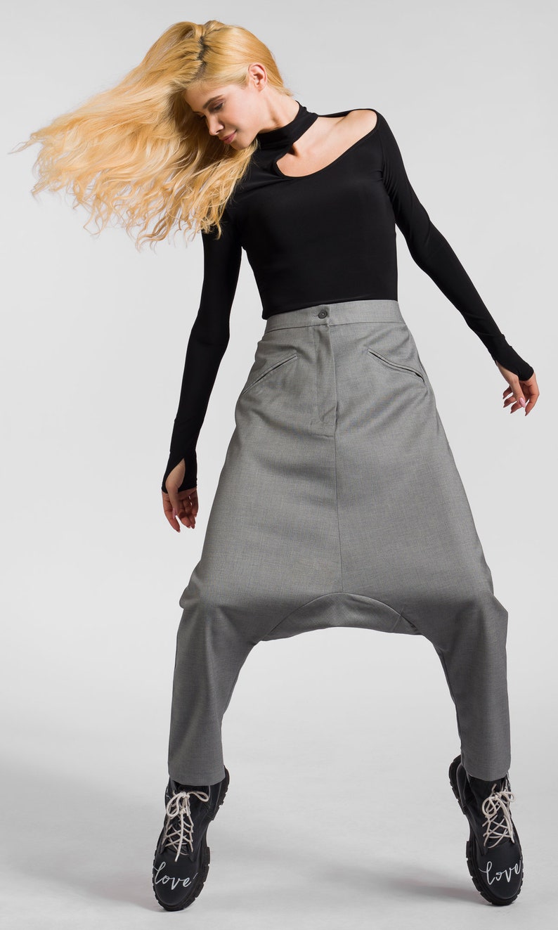 May include: A woman wearing a black long-sleeved shirt with a cut-out neckline and gray, loose-fitting pants. She is wearing black shoes with the word "love" written on them.