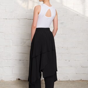 Pode incluir: Uma mulher vestindo um top branco sem mangas com um decote nas costas em forma de fechadura e uma saia preta em camadas. Ela est&aacute; usando t&ecirc;nis preto e branco com um cora&ccedil;&atilde;o vermelho e a palavra "with" em um sapato.