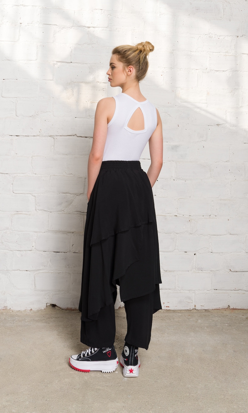 Pode incluir: Uma mulher vestindo um top branco sem mangas com um decote nas costas em forma de fechadura e uma saia preta em camadas. Ela est&aacute; usando t&ecirc;nis preto e branco com um cora&ccedil;&atilde;o vermelho e a palavra "with" em um sapato.
