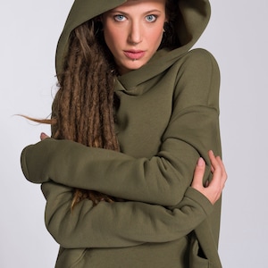 May include: A woman wearing a green hooded sweatshirt with long brown dreadlocks. The sweatshirt has a large pocket on the front.