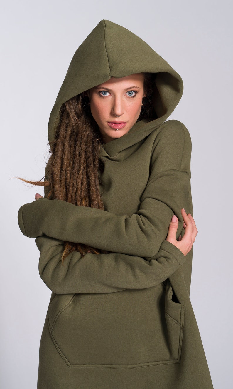 May include: A woman wearing a green hooded sweatshirt with long brown dreadlocks. The sweatshirt has a large pocket on the front.